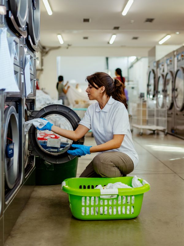 A worker in a commercial laundry facility handles clean linens with care, demonstrating the efficiency and professionalism of large-scale linen management operations. The scene includes industrial washing machines and organized storage systems.