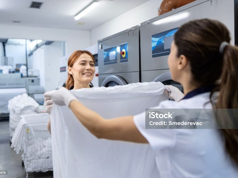 Professional female workers folding clean laundry together after drying process.