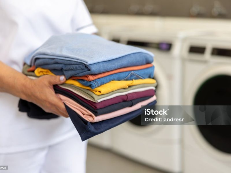 Close-up on a maid holding folded clothes at a laundromat - domestic life concepts